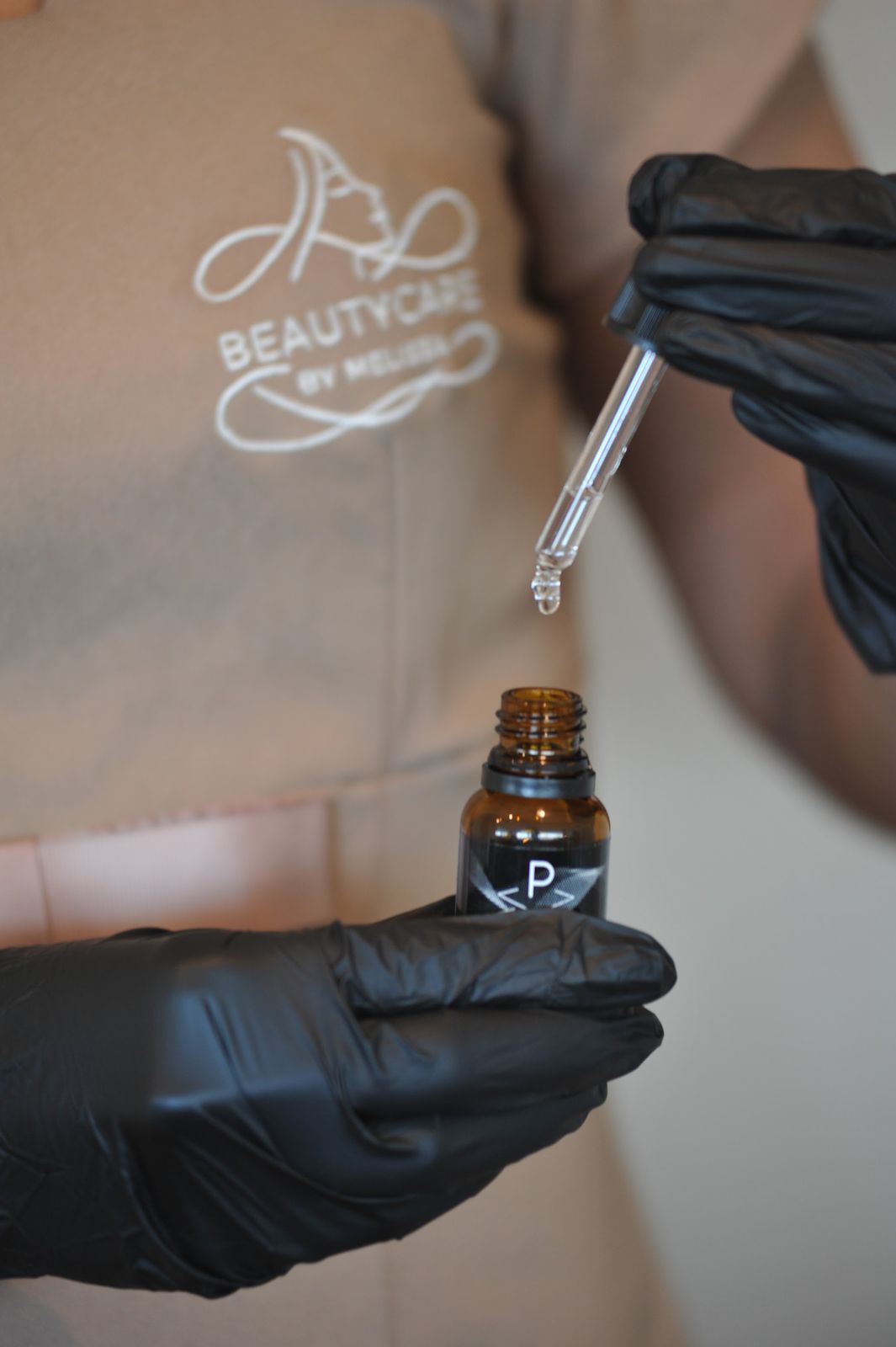 Handen in handschoenen met een pipet boven een flesje serum